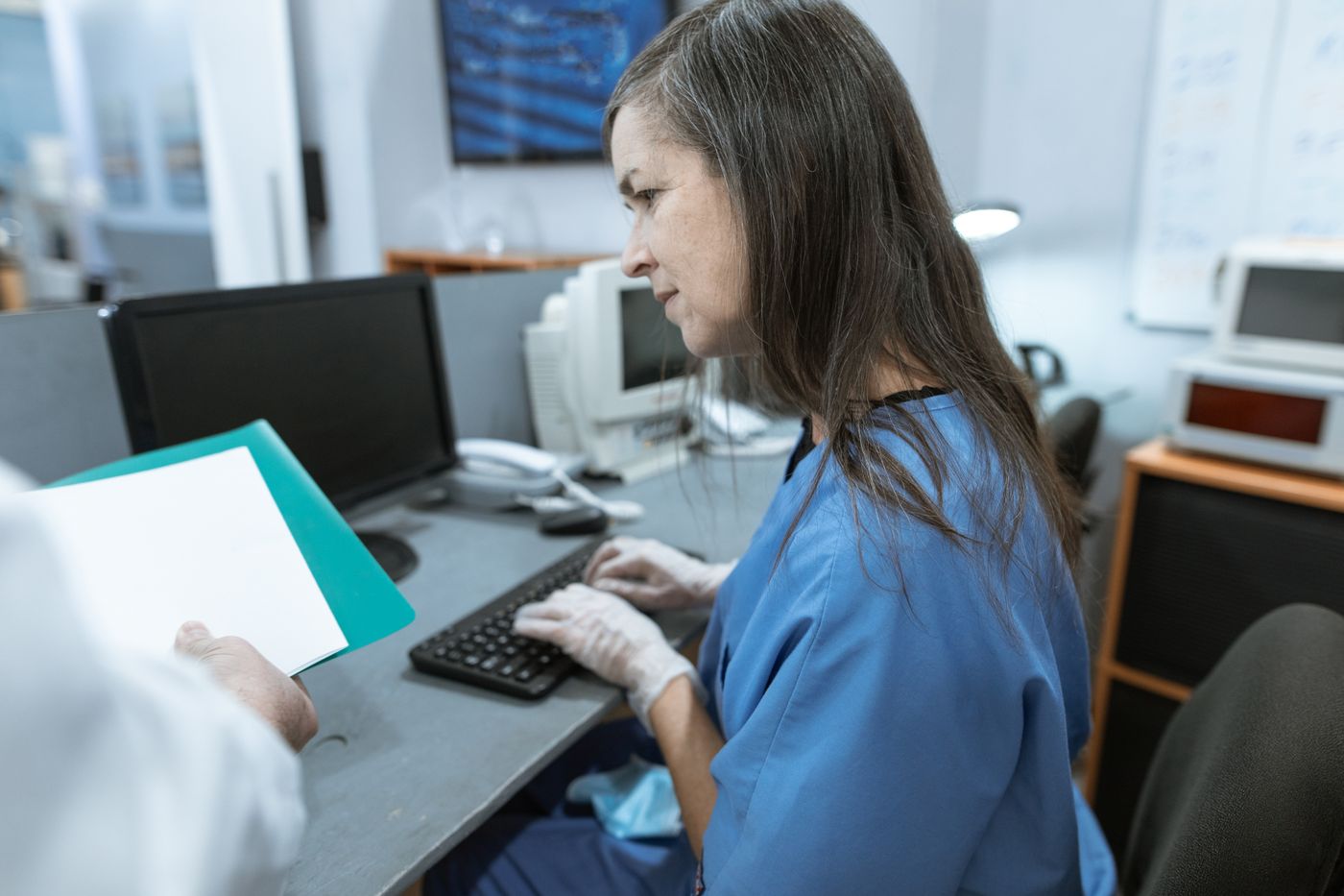 Healthcare worker in scrubs typing at a medical office workstation