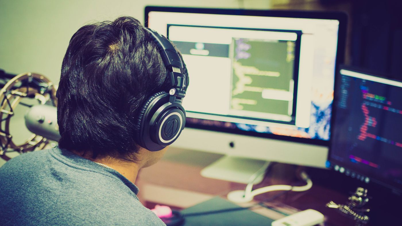 Programmer wearing headphones writing code at a dual-monitor workstation