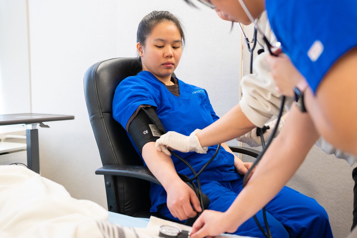 Healthcare worker in scrubs checking a patient’s blood pressure in a clinic