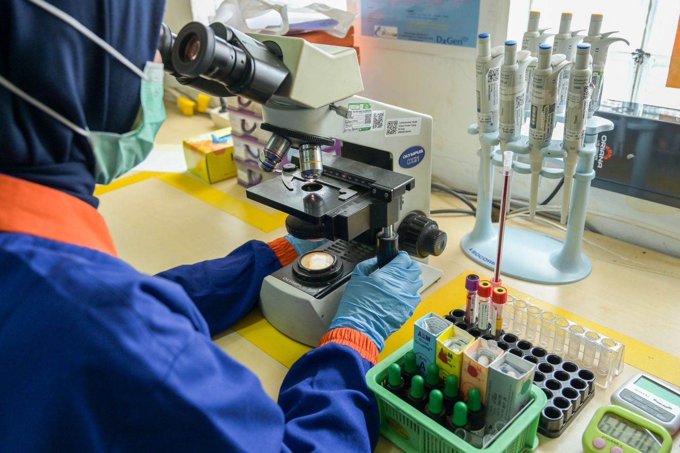 Laboratory technician examining samples under a microscope next to blood sample tubes