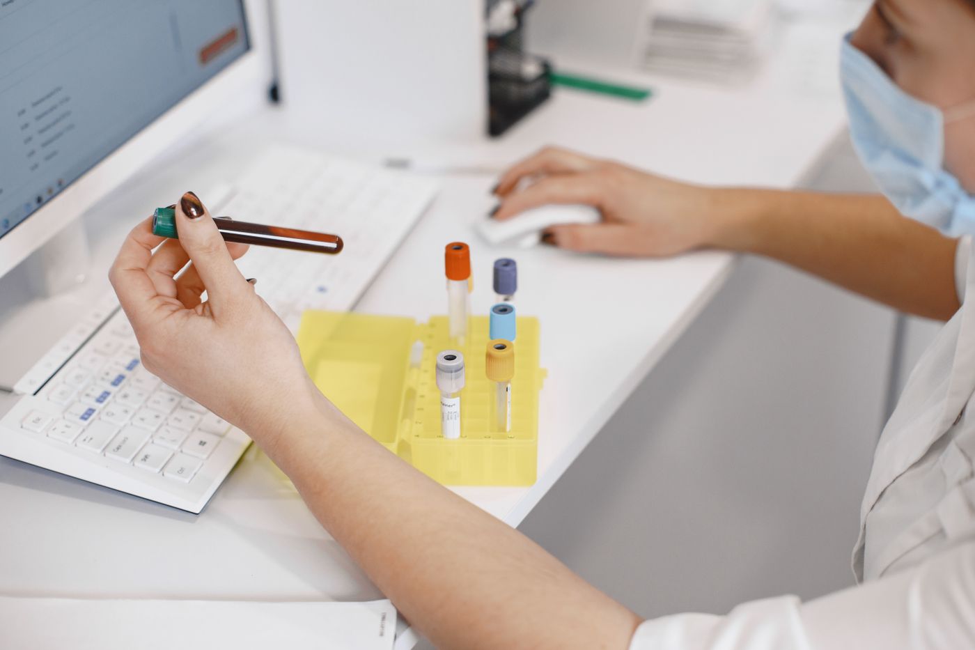 Laboratory technician handling blood sample tubes at a lab workstation
