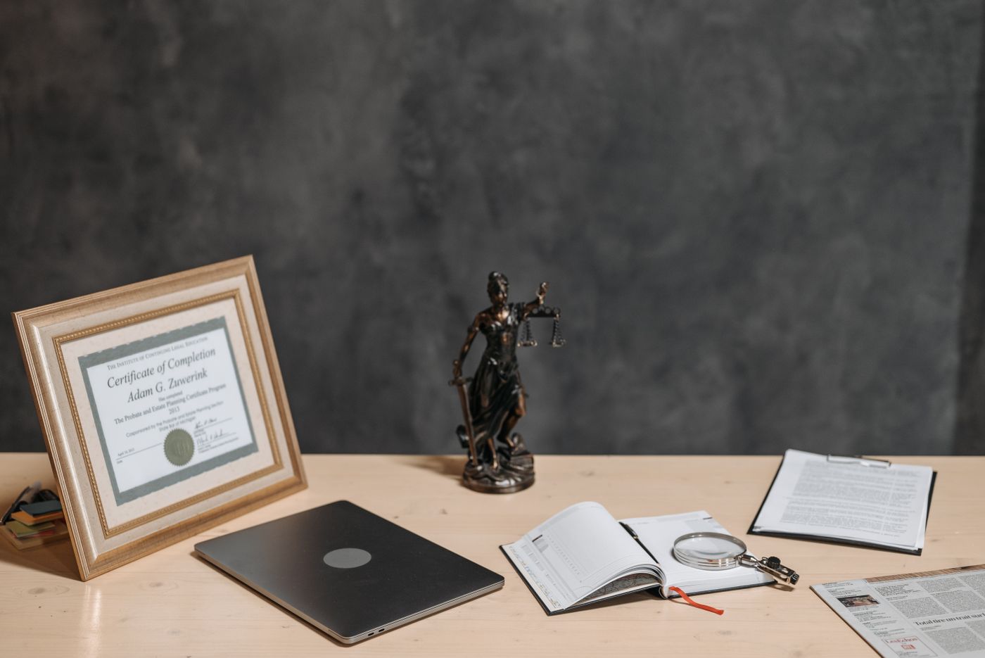 Law office desk with a scales of justice statue, framed diploma, laptop, and case documents